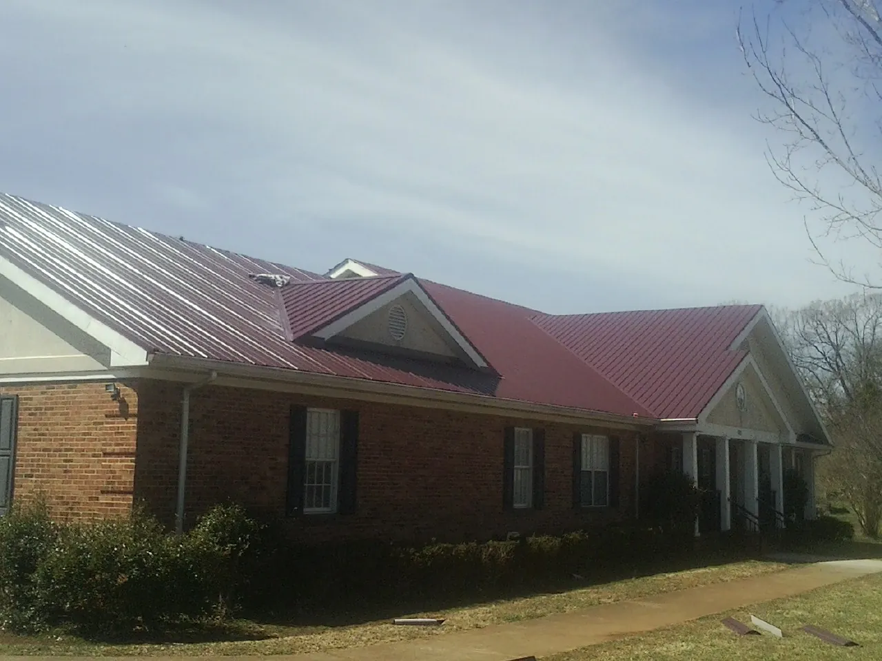 Red metal roof with gabled entries on a long brick building, from a Hail Damage Roof Repair job in Chickasha