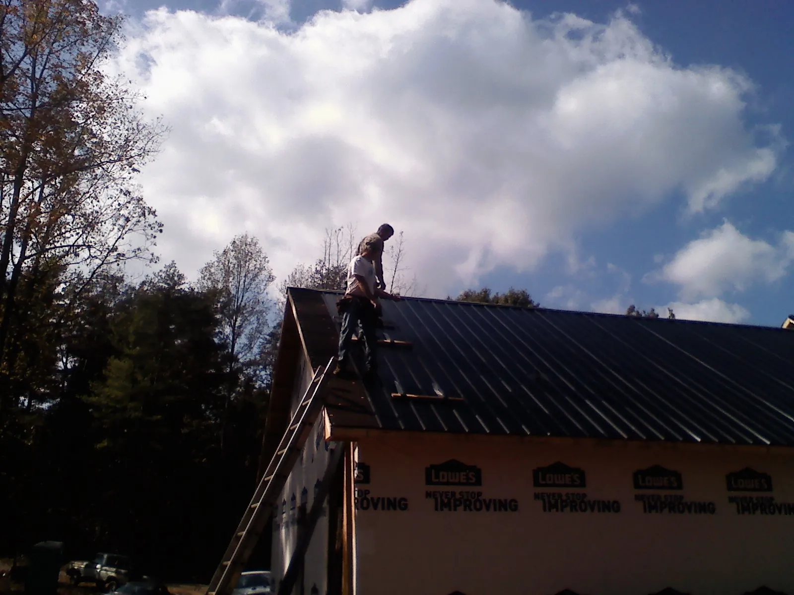 Roofer fastening dark metal panels high against a cloudy sky, from a Roof Inspection job in Chickasha