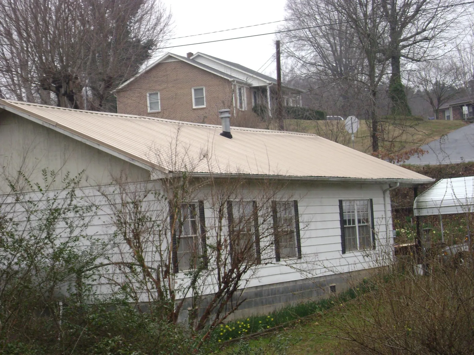 Tan metal roof on a white sided house set into a hillside — Commercial Roofing by Roofing Brothers in Chickasha