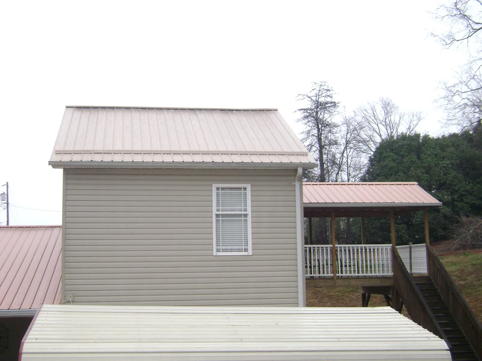 Tan metal roofs on a two story addition and attached porch, from a Roof Replacement job in Chickasha